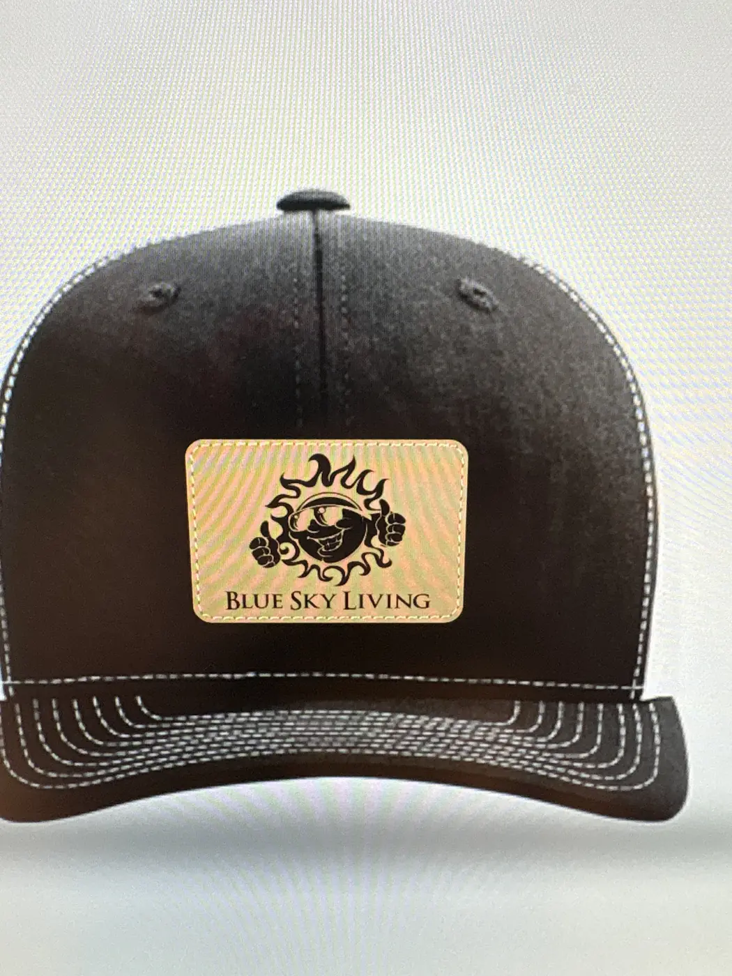 Black trucker hat with a leather Blue Sky Living patch on the front